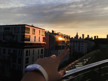 Midsection of person holding buildings in city against sky during sunset