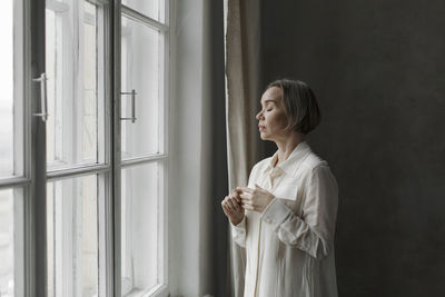 Woman with eyes closed standing in front of window