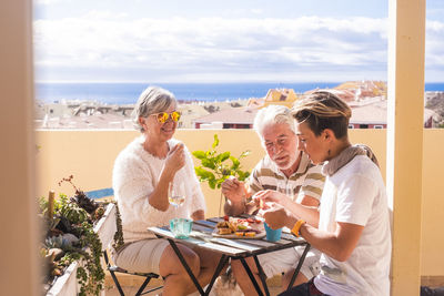 Senior couple having food and drinks with grandson at table in balcony