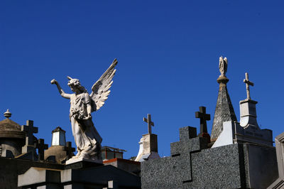 Low angle view of statue and cross in cemetery against clear blue sky