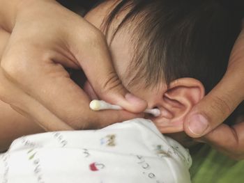 Cropped hands of father cleaning son ear with cotton swab at home