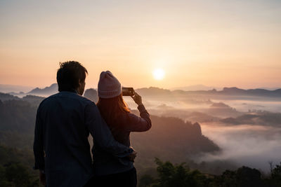 Rear view of man standing on mountain against sky during sunset