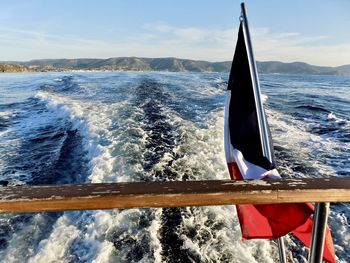 Watching the waves from the stern of a boat. coastline in the background, french flag floating.
