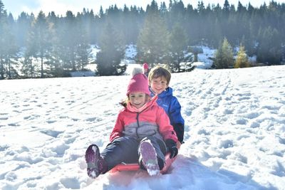 Boy sitting on snow covered landscape during winter