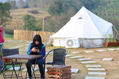 Young woman using smart phone while sitting on chair at campsite