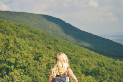 Rear view of young woman with backpack looking at mountains against sky