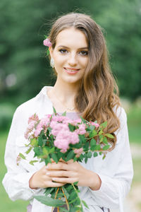 Young girl stand at park background with bouquet of pink spireya flowers