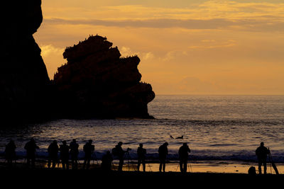 Silhouette people on beach against sky during sunset