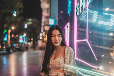 Portrait of woman standing on illuminated street at night