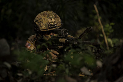 Soldier holding rife by plants in forest