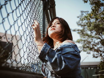 Low angle view of woman looking through chainlink fence