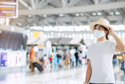 Woman wearing flu mask and hat standing at airport