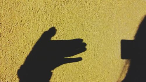 Shadow of person hand on yellow wall