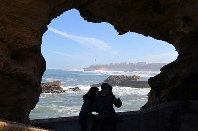 People on rock by sea against sky