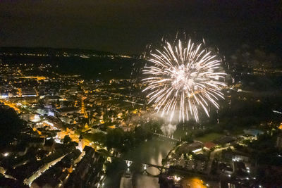 Firework display over illuminated city against sky at night