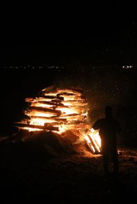 Rear view of silhouette man standing against illuminated fire at night