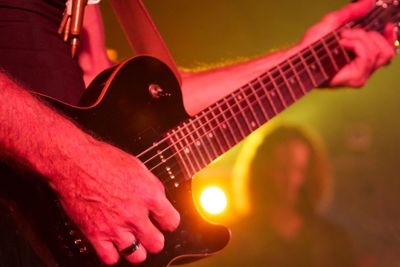 Midsection of guitarist performing at illuminated music concert