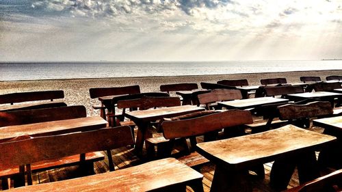 Empty chairs and table at beach against sky