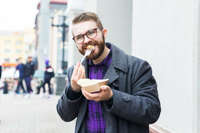 Portrait of young man holding ice cream standing outdoors