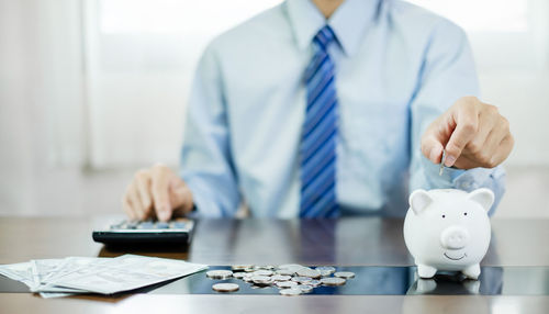 Midsection of businessman putting coin in office