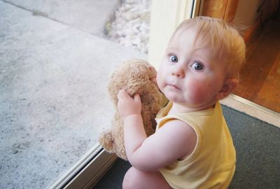 Portrait of cute baby holding teddy bear while crouching in front of door