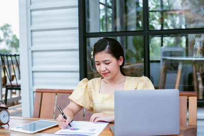 Young woman using mobile phone while sitting on table