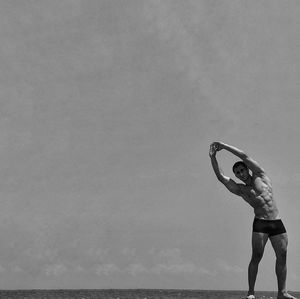 Full length of shirtless man exercising against sky