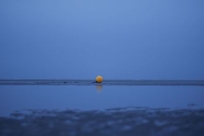 Ball floating on sea against clear blue sky