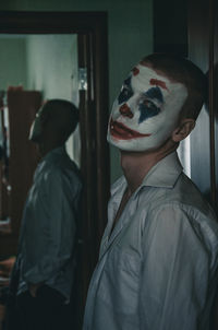 Portrait of young man with face paint standing against wall