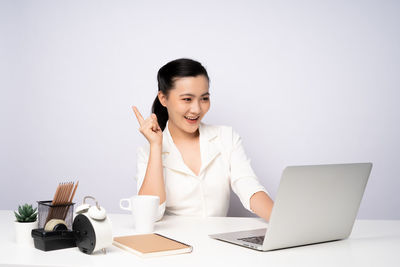 Smiling young woman using laptop on table against white background