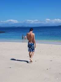 Full length of rear view of shirtless man walking at beach against sky