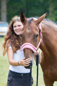 Portrait of happy woman with horse standing on field