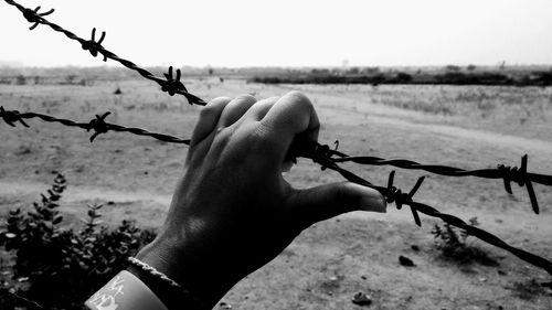Close-up of hand holding barbed wire against clear sky