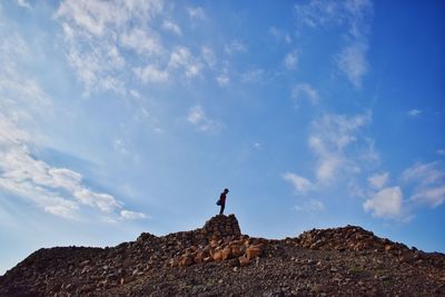 Low angle view of man standing on rock against sky