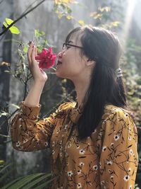 Young woman smelling red rose on plant