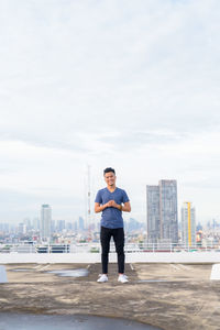 Full length portrait of young man standing on city against sky