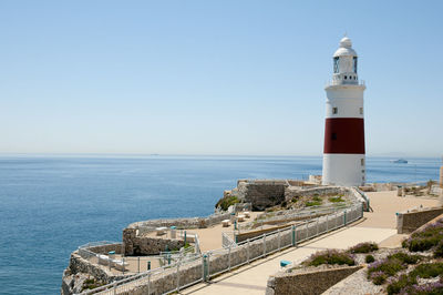 Lighthouse by sea against buildings against clear sky