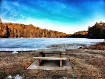 Empty bench by lake against sky during winter