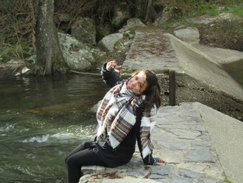 Portrait of young woman showing peace sign while sitting on lakeshore