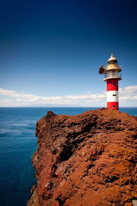 Lighthouse on rock by sea against blue sky