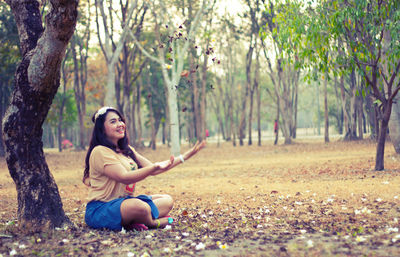 Side view of woman playing with leaves while sitting on field