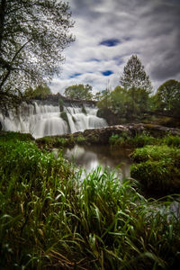 Scenic view of waterfall by trees against sky