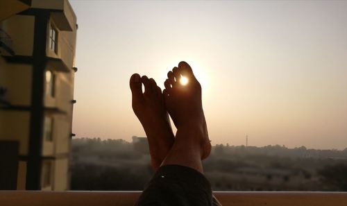 Low section of woman relaxing in city against sky during sunset