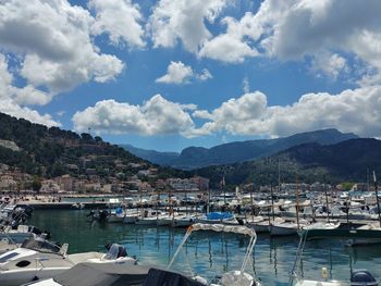 Sailboats moored at harbor against cloudy sky