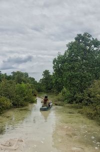 People sitting on riverbank against sky