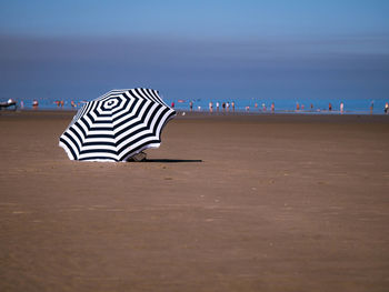 View of striped umbrella on sand at beach against sky during sunny day