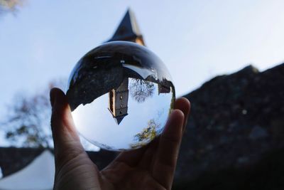 Close-up of hand holding crystal ball against sky