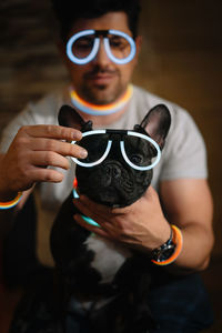 Midsection of man with neon glasses holding french bulldog dog