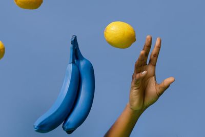 Low angle view of hand holding banana against clear blue sky