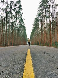 Rear view of man standing on empty road amidst trees
